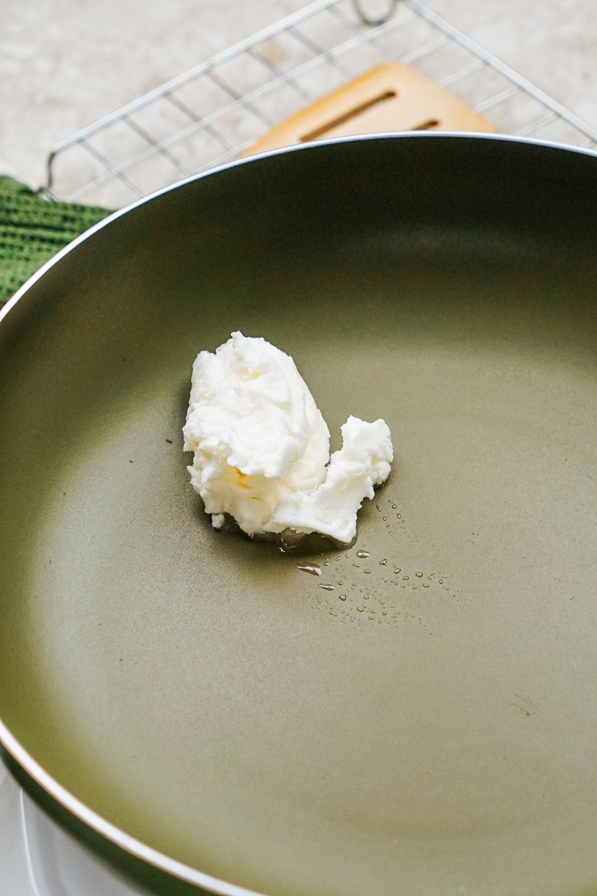 A dollop of white cream nestles in a green frying pan on the countertop, ready to transform ordinary ingredients into a delicious filling for stuffed peppers.