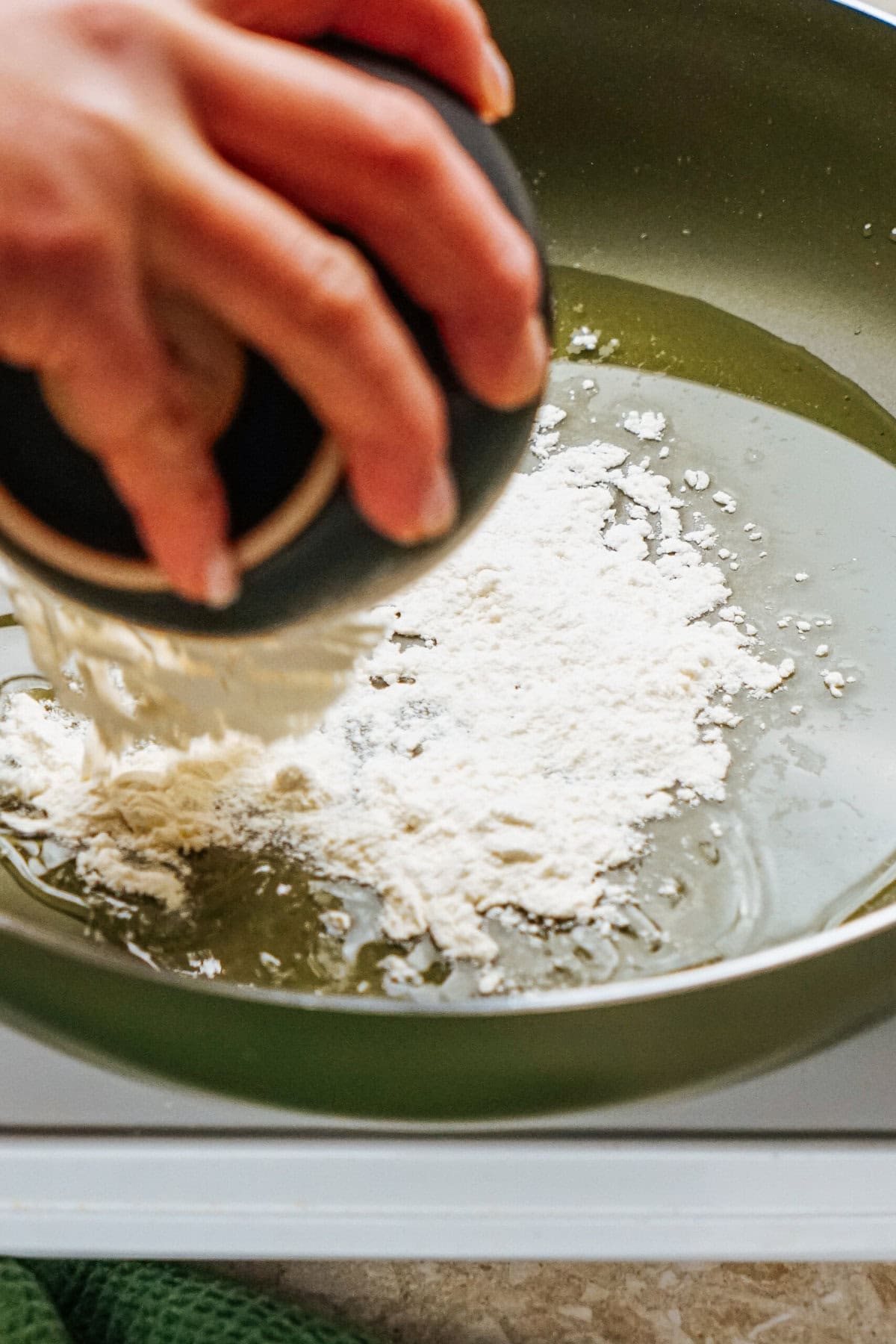 A person adds a scoop of flour from a black bowl into a pan with oil, beginning the savory foundation for their delicious stuffed peppers.