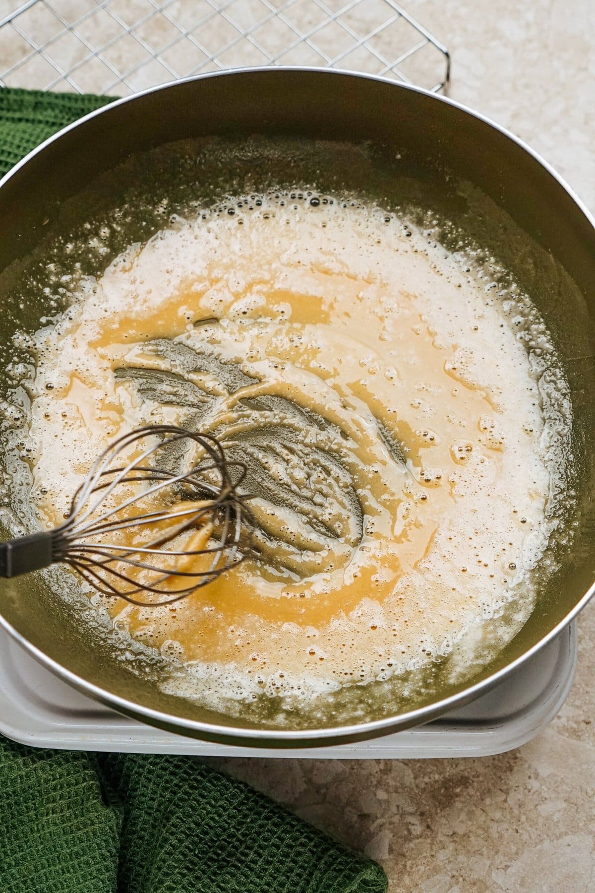 A whisk stirs light brown roux in a pan, ready to create the perfect sauce for stuffed peppers, with a green cloth nearby.