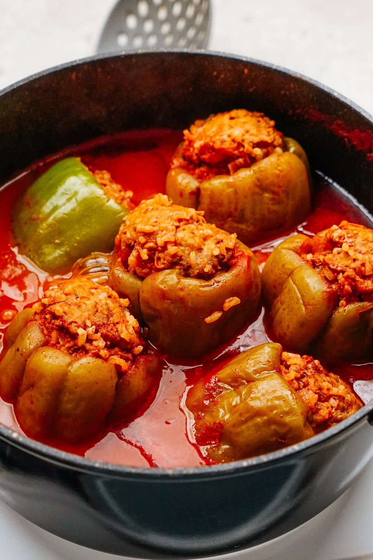 A pot brims with a rich tomato-based sauce, cradling savory stuffed peppers that promise a burst of flavor in every bite.