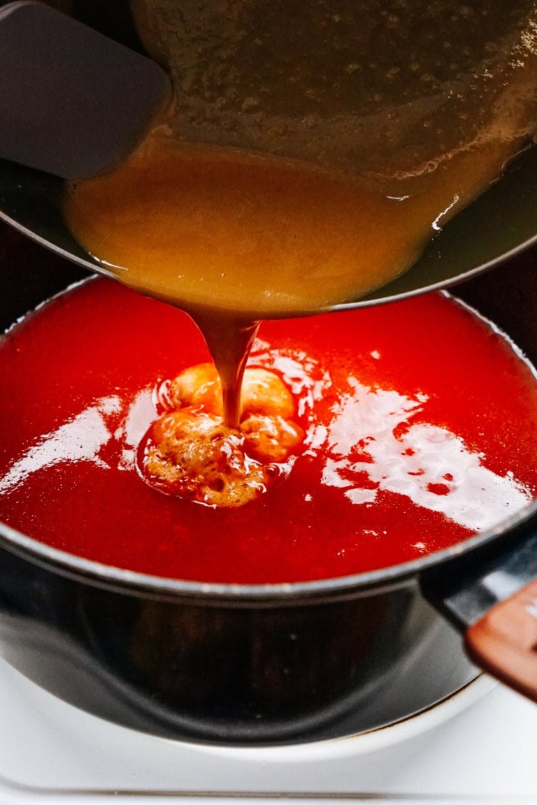 A yellow-orange sauce is being poured into a pot containing a red liquid, likely forming an emulsion as it blends, reminiscent of the rich flavors you'd find in stuffed peppers.