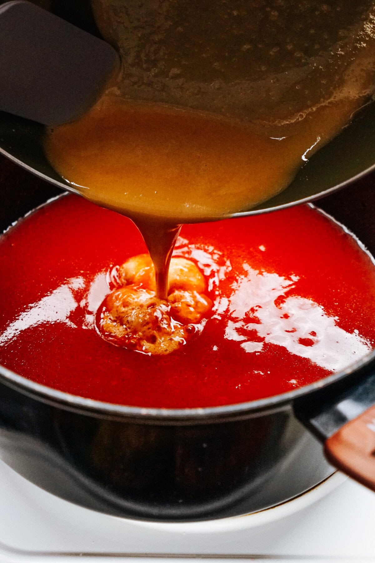 A yellow-orange sauce is being poured into a pot containing a red liquid, likely forming an emulsion as it blends, reminiscent of the rich flavors you'd find in stuffed peppers.