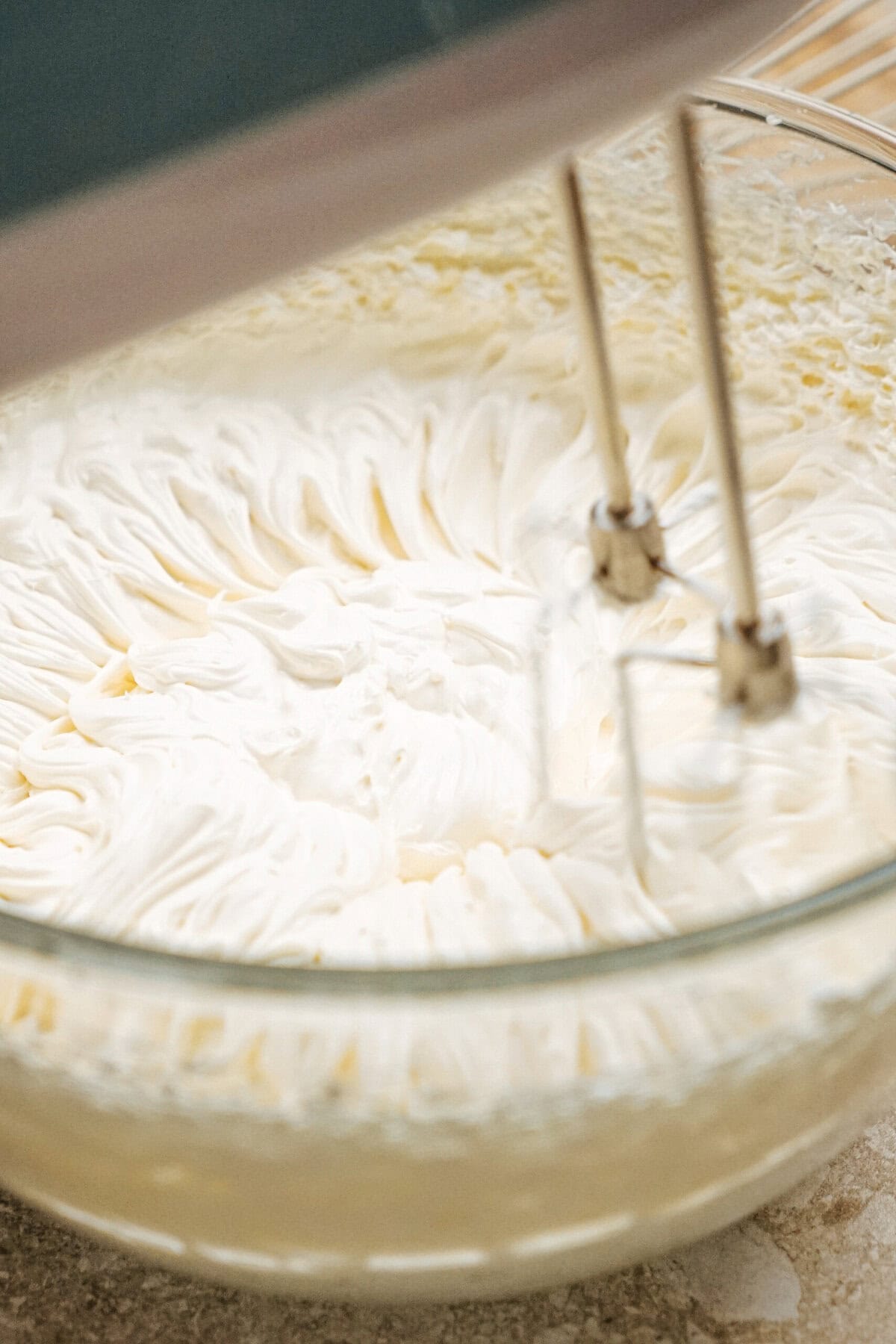 Close-up of an electric mixer beating fluffy white cream in a glass bowl.