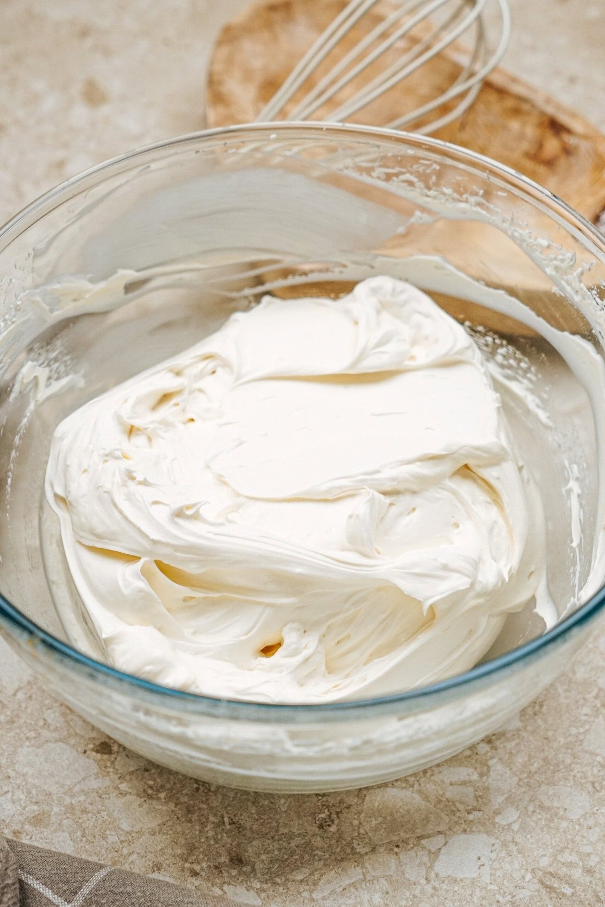 A glass bowl filled with smooth, creamy whipped mixture on a countertop with a wooden spoon and whisk nearby.