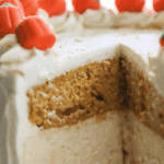 A close-up of a layered cake with white frosting, decorated with small pumpkin-shaped candies, and a slice missing to show the inside.