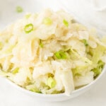A white bowl filled with creamy mashed potatoes and shredded cabbage, garnished with chopped green onions.