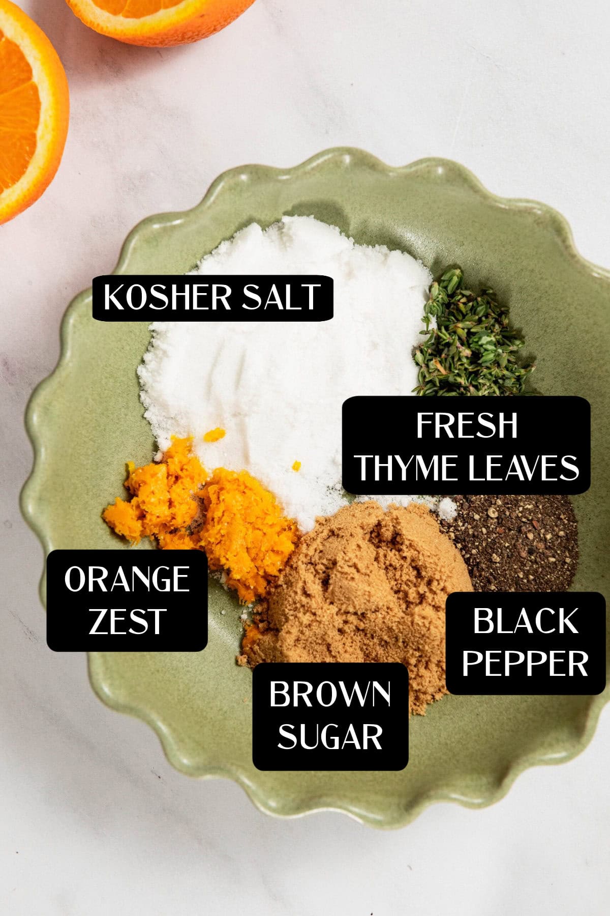 A green bowl containing kosher salt, fresh thyme leaves, black pepper, brown sugar, and orange zest—each ingredient labeled with text—shows the essentials for an Easy Turkey Dry Brine Recipe.