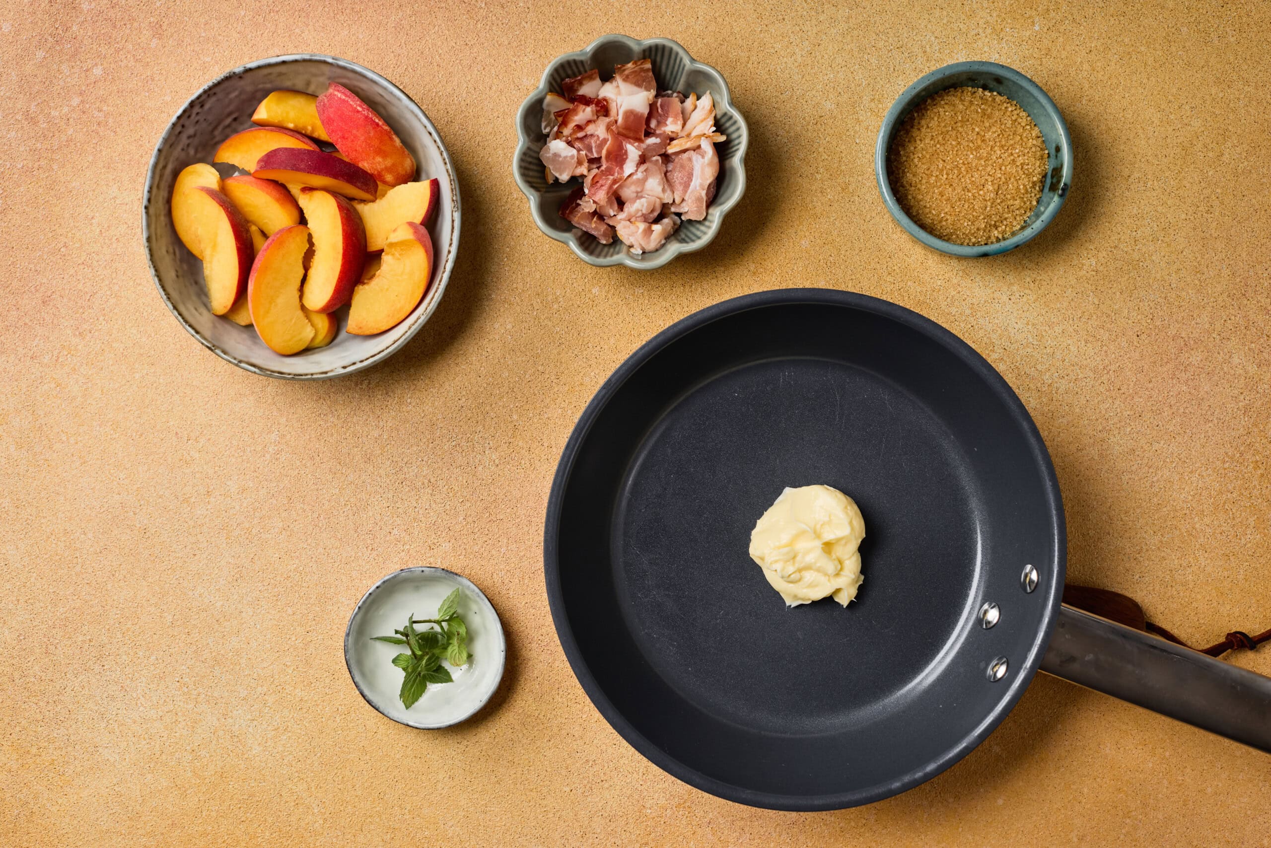 Fresh peach slices, chopped bacon, brown sugar, butter, and fresh herbs ready for cooking.