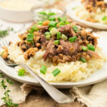 A plate of rice topped with shredded meat, black-eyed peas, and chopped green onions, with a fork on the side.