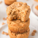 A stack of three peanut butter muffins with peanut butter chips, the top muffin has a bite taken out of it.