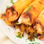 A plate of golden-brown, crispy taquitos filled with shredded meat, garnished with chopped parsley.