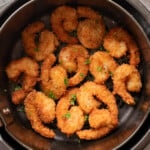Breaded shrimp arranged in a single layer in an air fryer basket, garnished with chopped parsley.