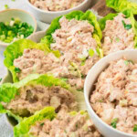 Tuna salad served in lettuce leaves on a plate, with two bowls of extra tuna salad and chopped green onions in the background.