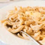 A close-up of a plate of creamy pasta garnished with black pepper, with a fork resting on the plate.