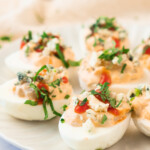 A plate of deviled eggs garnished with chopped herbs, crumbled cheese, and a drizzle of red sauce.