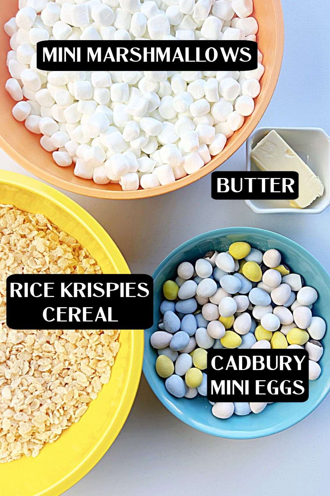 Bowls filled with mini marshmallows, Rice Krispies cereal, and Cadbury Mini Eggs alongside a dish of butter, everything you need to make festive Cadbury Rice Krispie Treat Eggs for Easter.