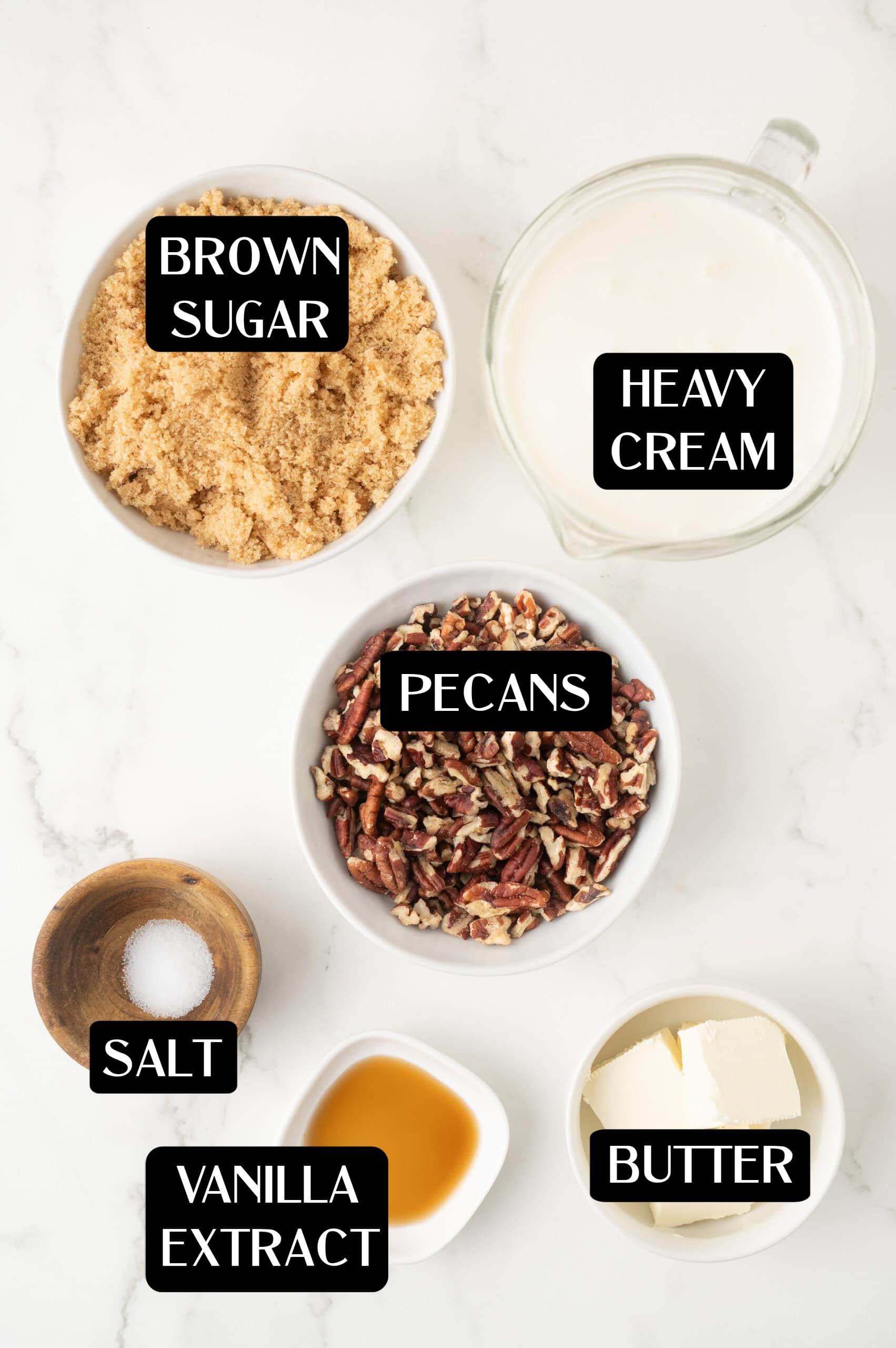 Top-down view of ingredients in bowls on a white surface, including brown sugar, heavy cream, pecans, salt, vanilla extract, and butter—each labeled—perfect for making homemade butter pecan ice cream.