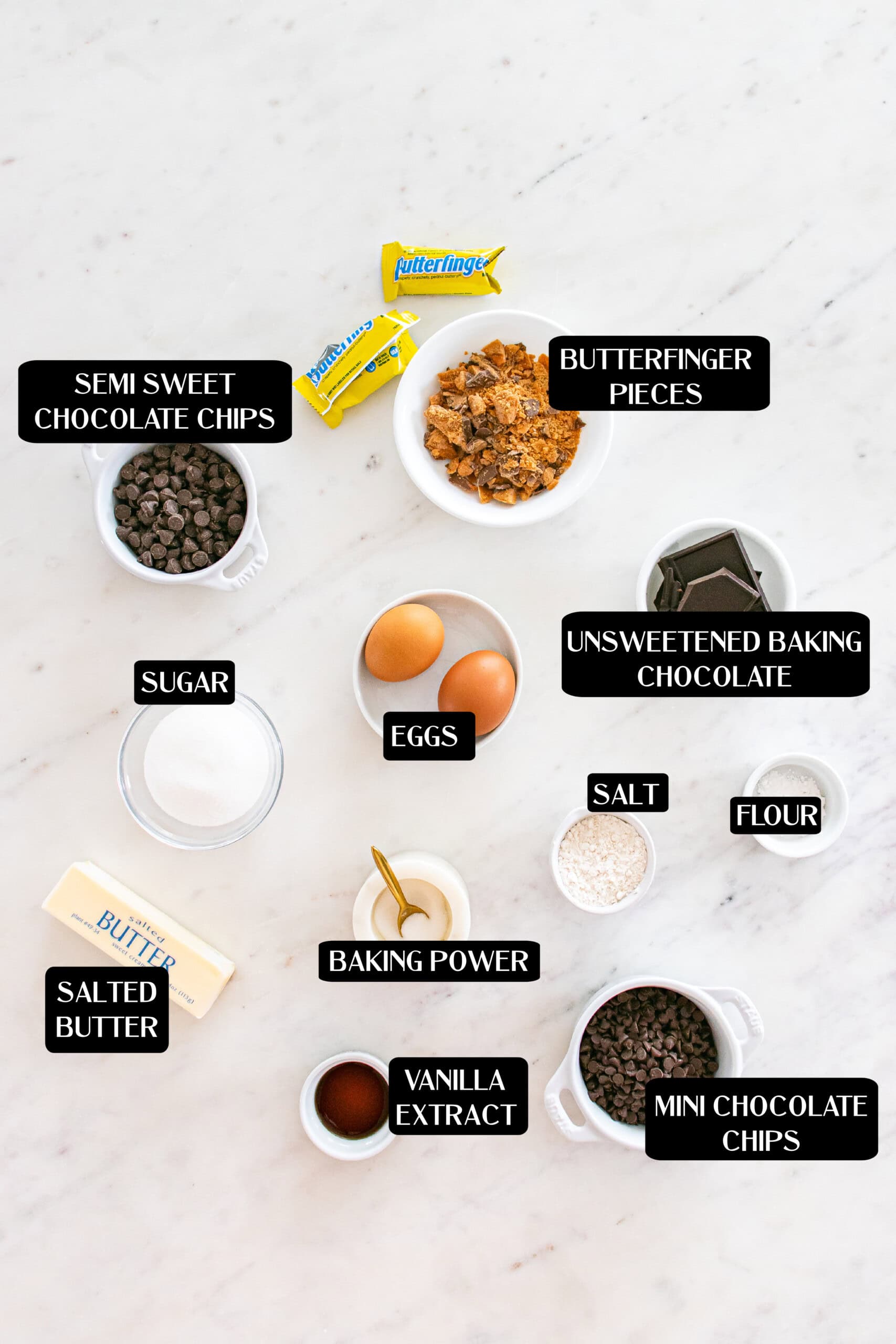 Various baking ingredients for Butterfinger Brownies, including semi-sweet chocolate chips, Butterfinger pieces, eggs, sugar, unsweetened baking chocolate, flour, salt, baking powder, vanilla extract, butter, and mini chocolate chips.