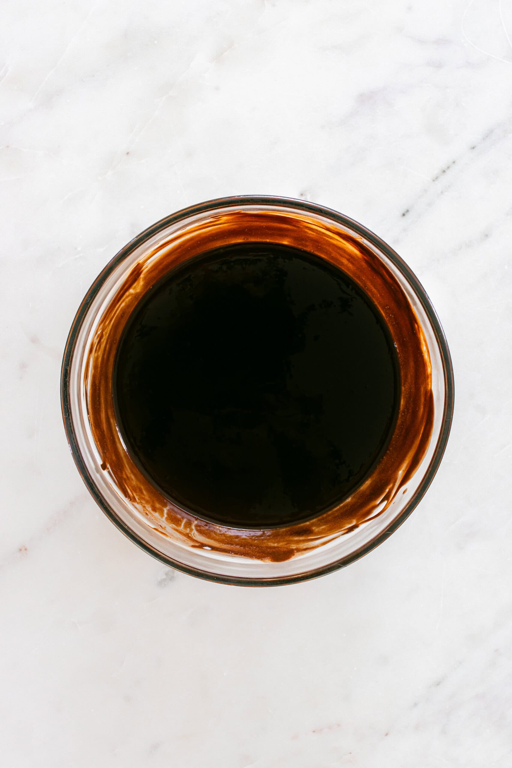 A glass bowl filled with a dark brown liquid, placed on a white marble surface.