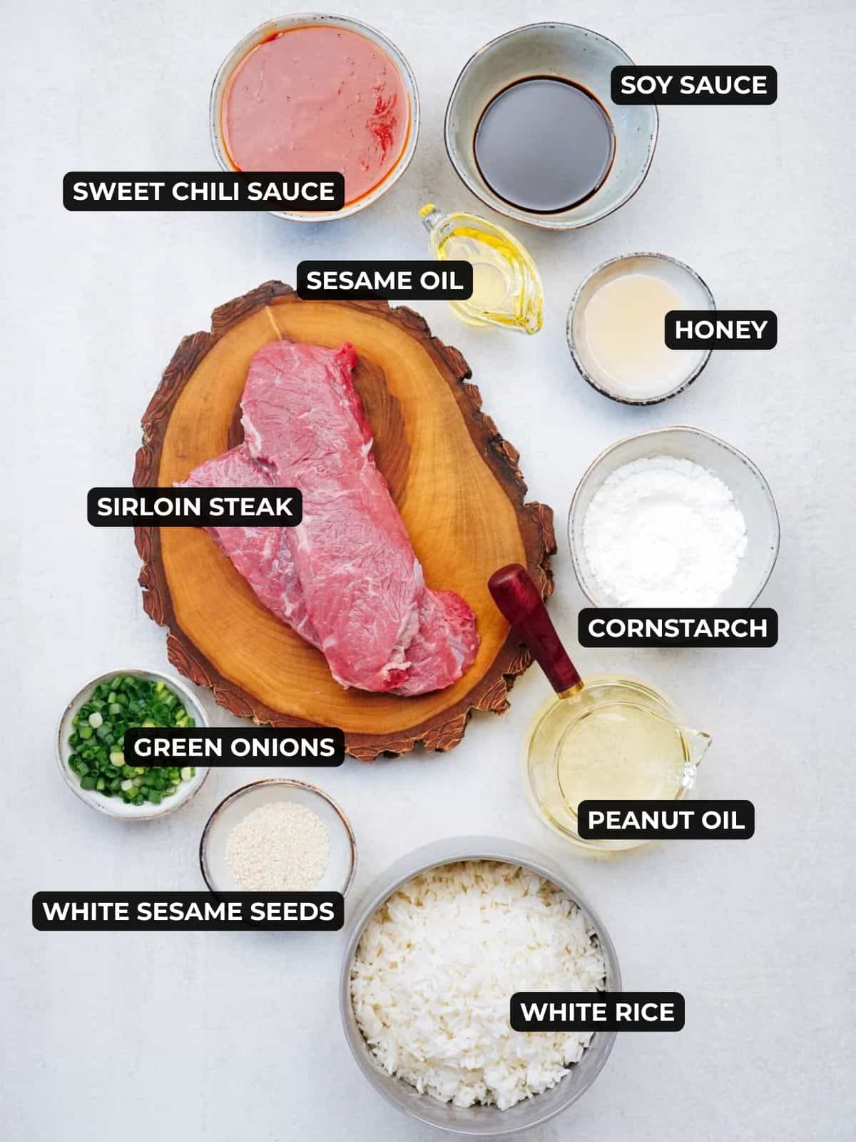 Ingredients for crispy sesame beef including sirloin steak, soy sauce, sesame oil, sweet chili sauce, honey, cornstarch, peanut oil, green onions, sesame seeds, peanut oil, and rice