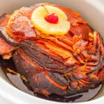 A delicious crockpot ham topped with a pineapple slice and a maraschino cherry, cooked to perfection in a slow cooker.