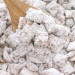 Puppy chow coated in powdered sugar served on a wooden spoon.