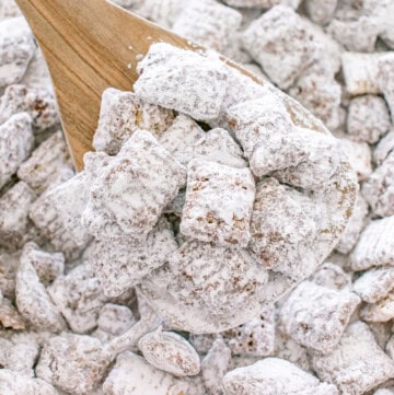 Puppy chow coated in powdered sugar served on a wooden spoon.