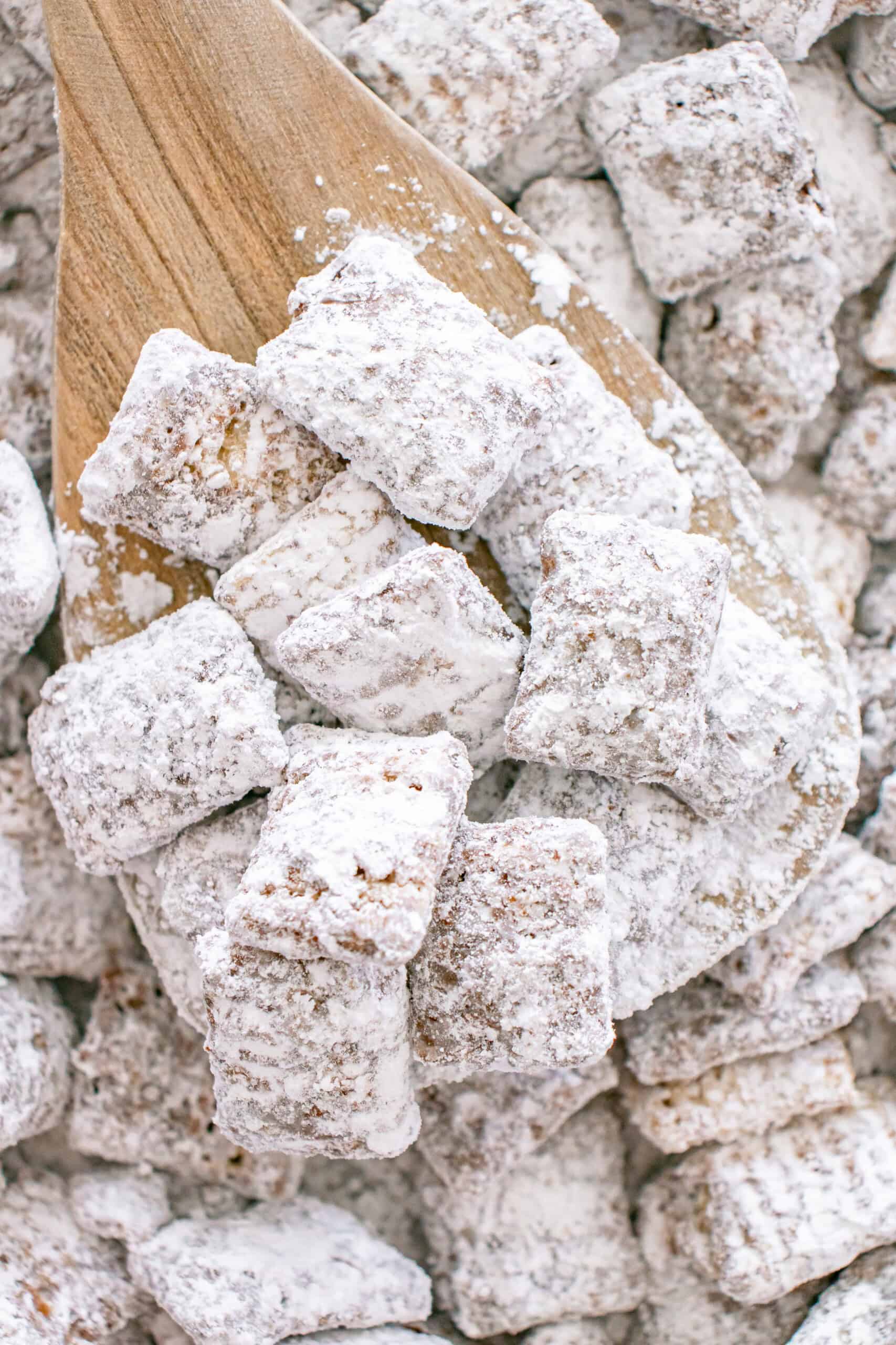 Puppy chow coated in powdered sugar served on a wooden spoon.
