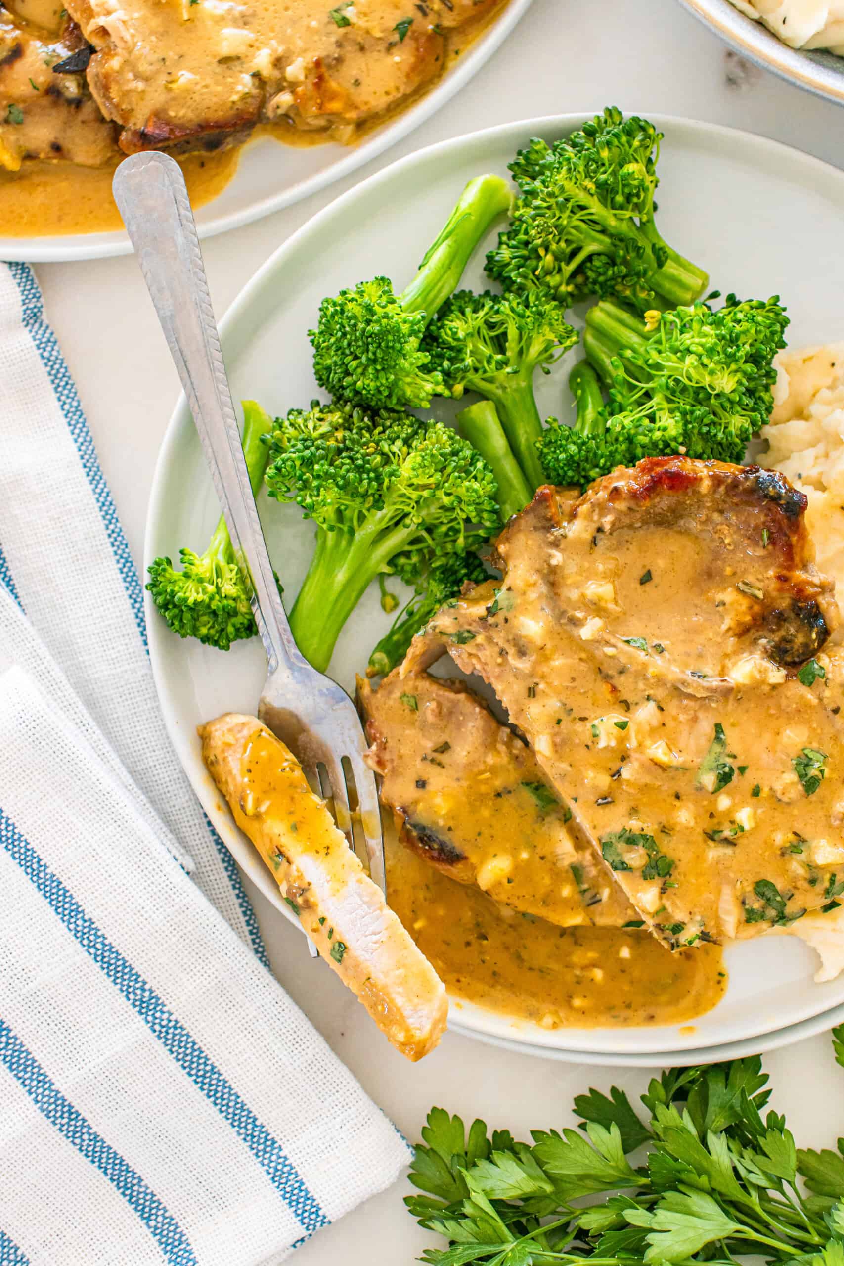 Delicious creamy pork chops served with fresh broccoli and mashed potatoes on a white plate.
