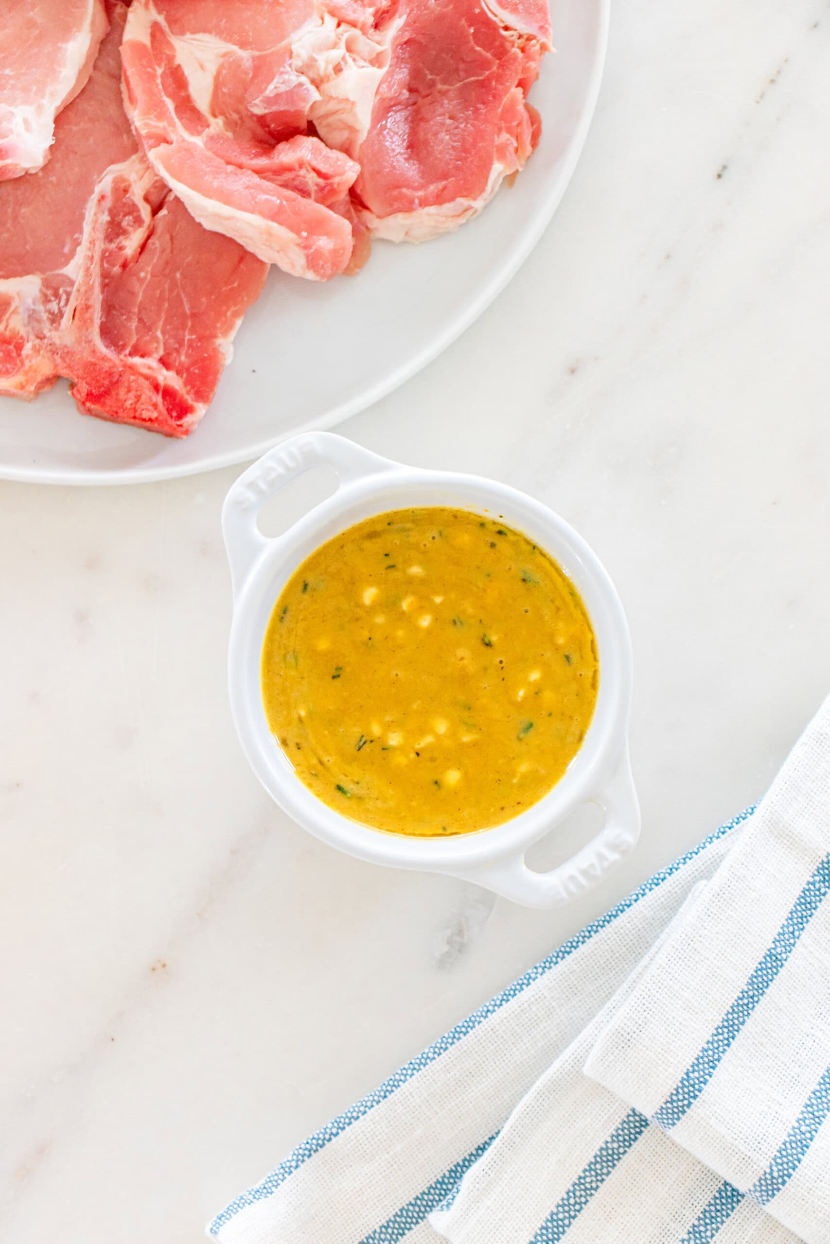 Pork chops with mustard herb sauce and raw pork on a white plate.