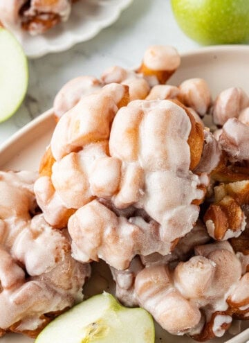 Apple fritters topped with a sweet glaze and served with fresh green apple slices.