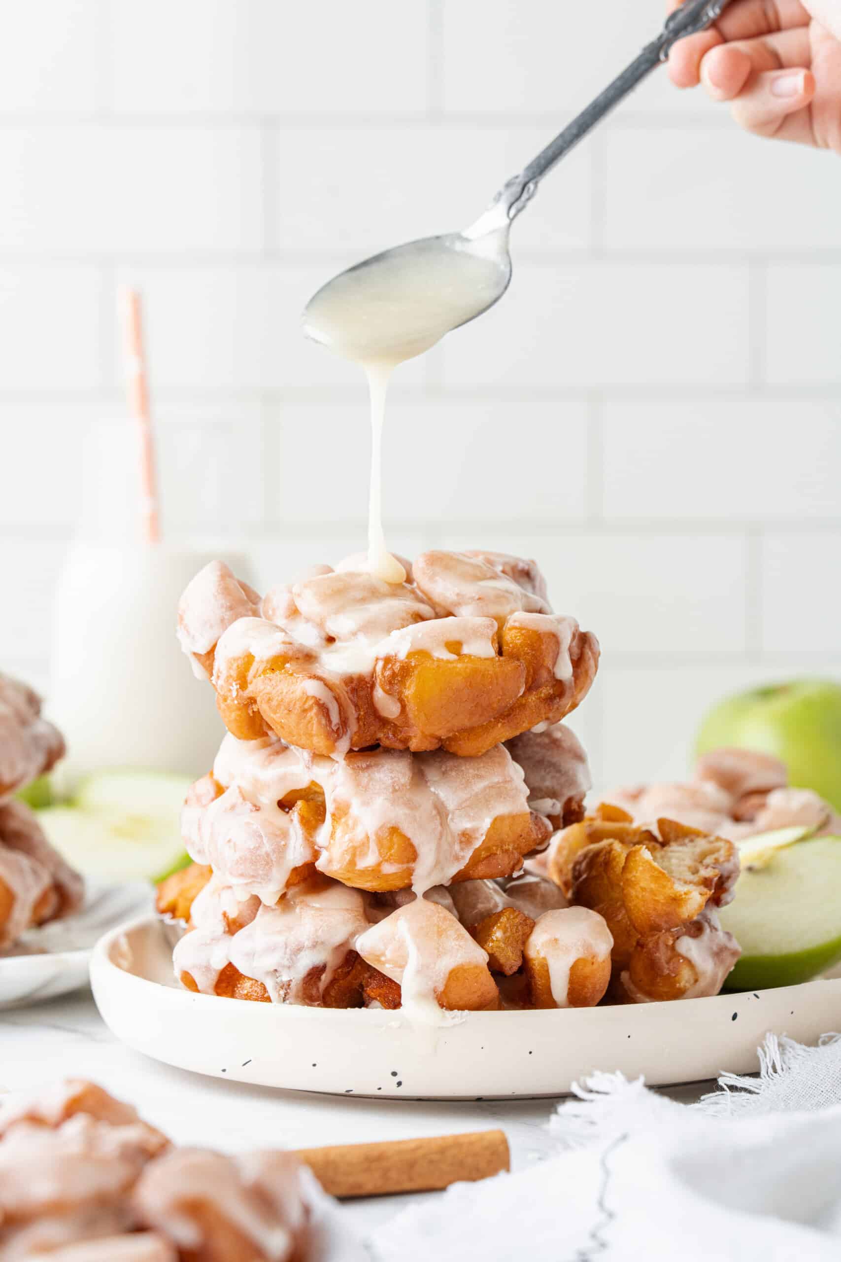 Stack of glazed apple fritters with extra vanilla glaze drizzled over the top.