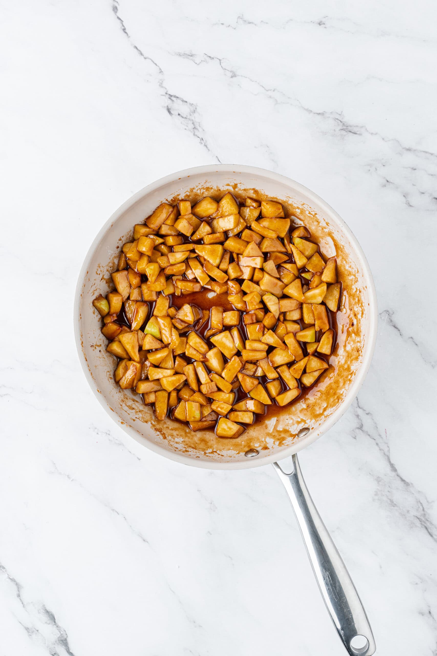 Cooked cinnamon apples in a caramel-like sauce in a skillet.
