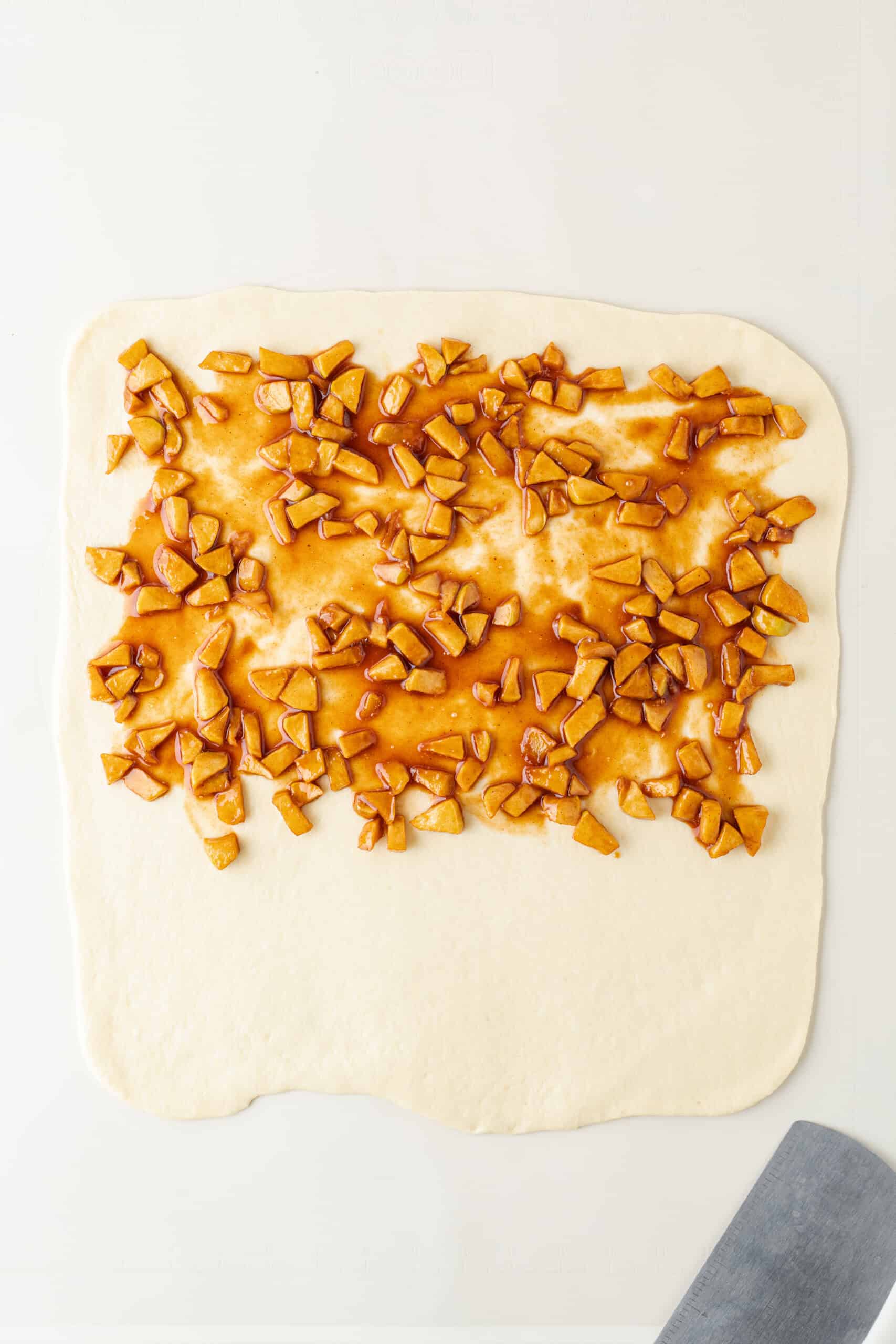 Cooked cinnamon apples spread over rolled apple fritter dough.