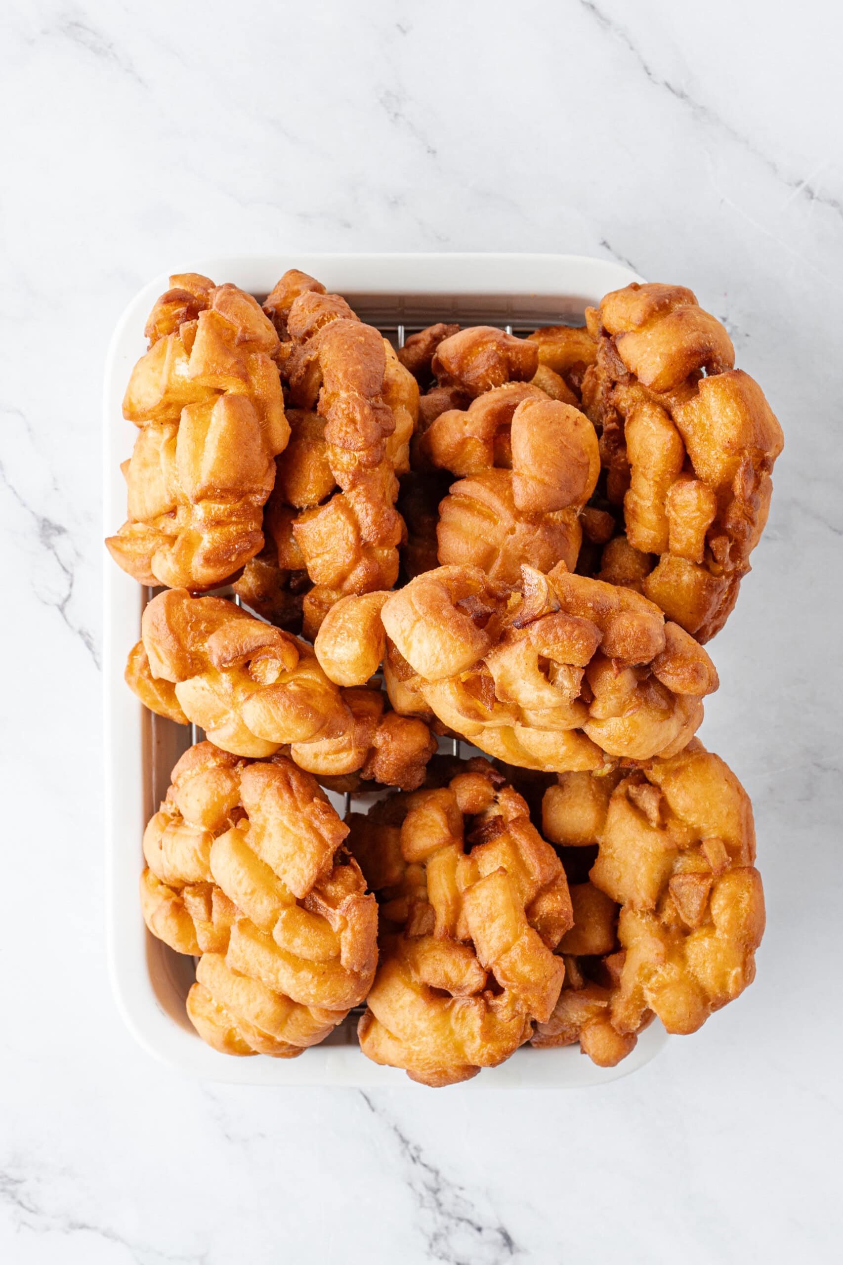 Freshly fried apple fritters cooling on a wire rack.