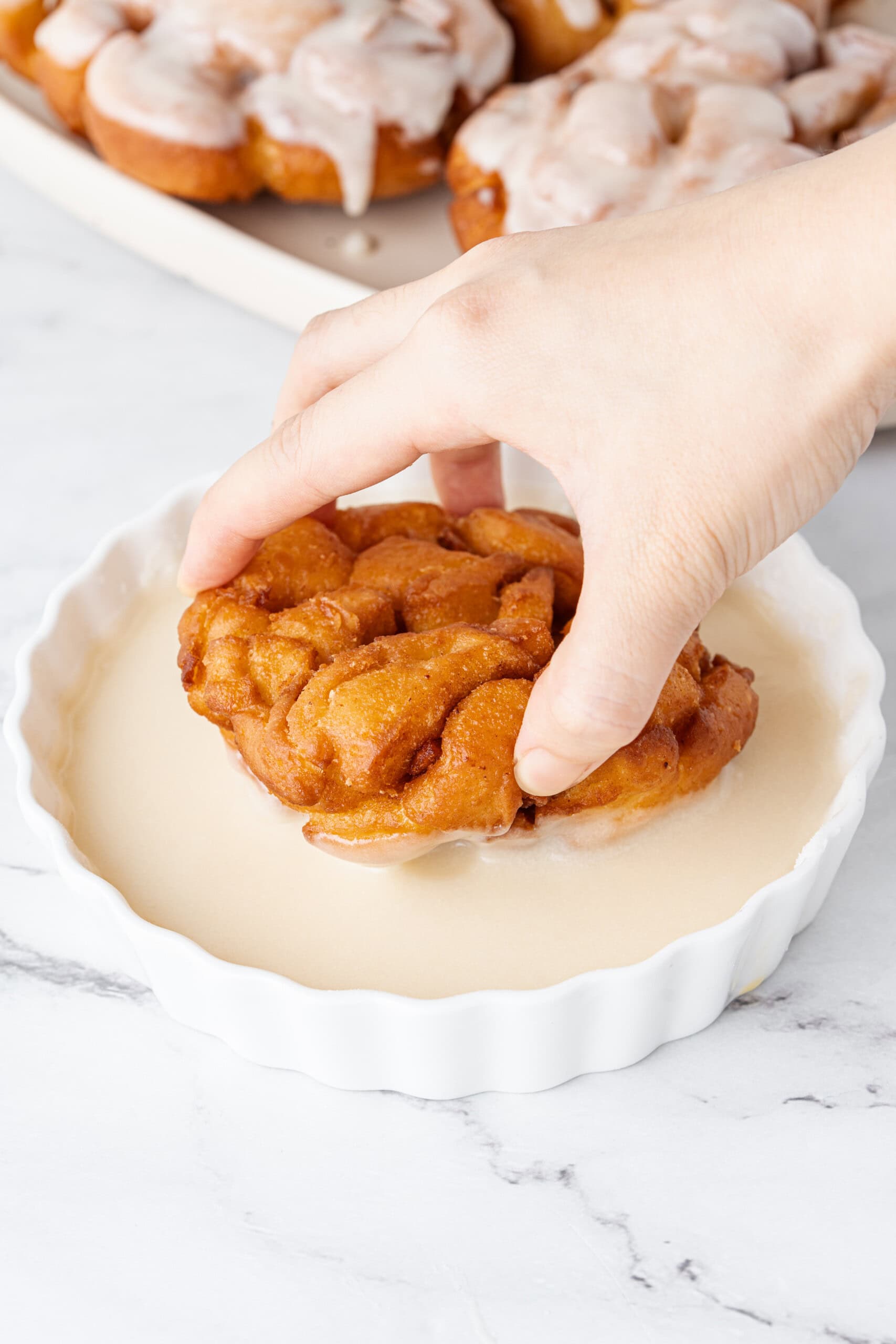 Dipping a freshly fried apple fritter into the glaze.