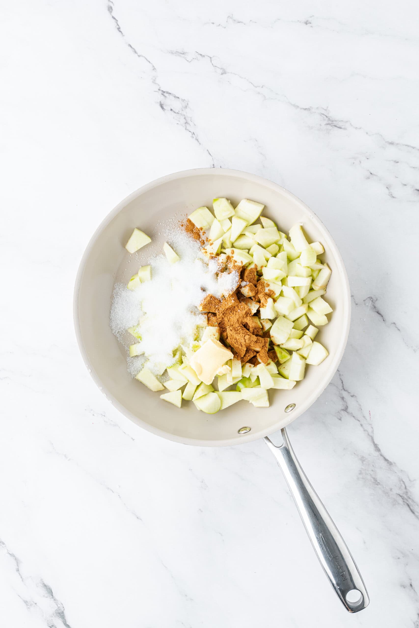 Chopped apples with sugar, cinnamon, and butter in a skillet.