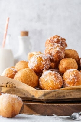 Golden brown donut holes coated in sugar and piled on a wooden serving board