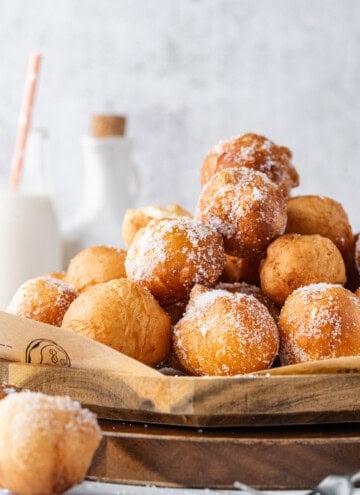 Golden brown donut holes coated in sugar and piled on a wooden serving board