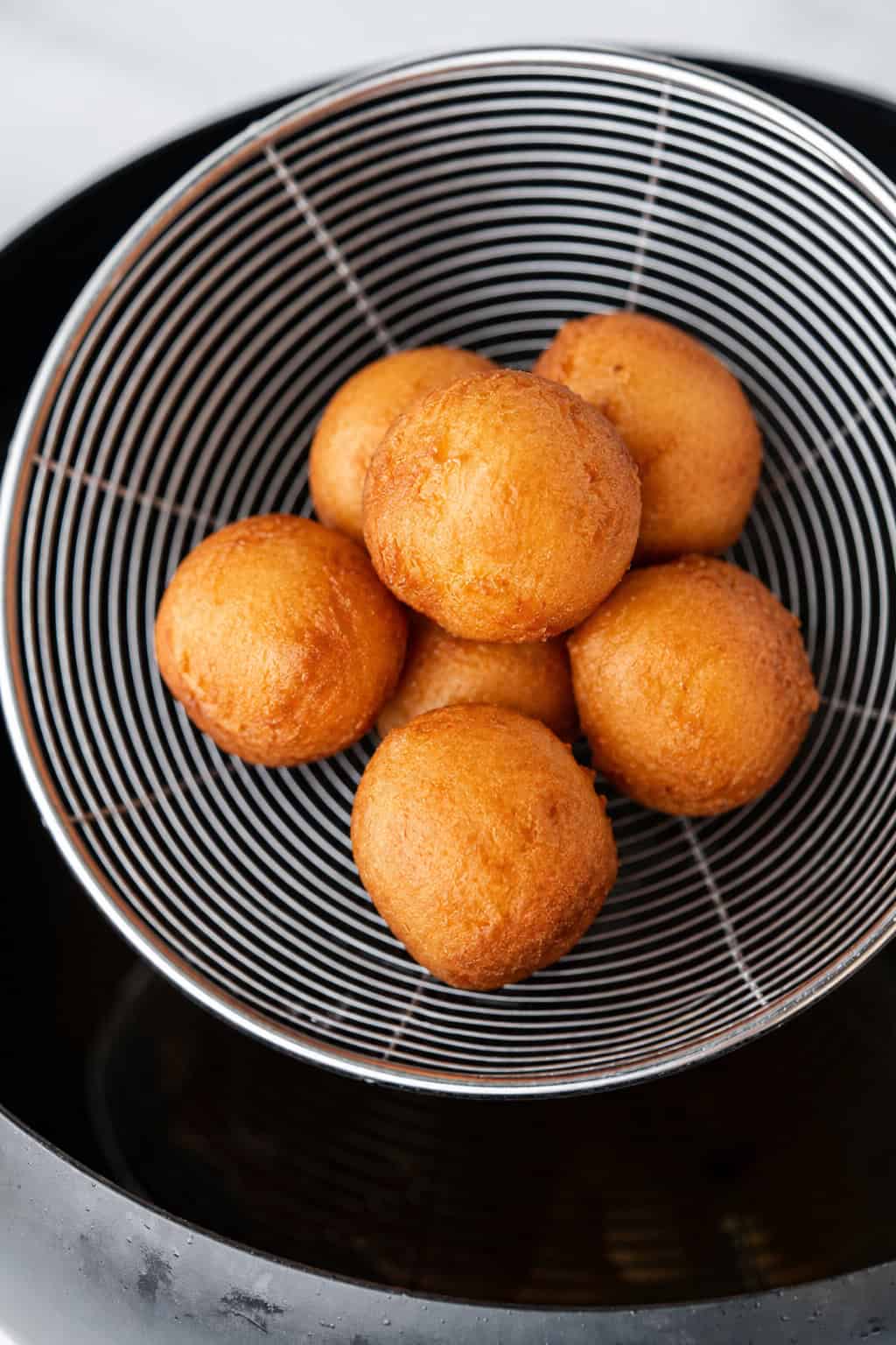 Golden brown donut holes draining in a wire skimmer above a pot of hot oil.