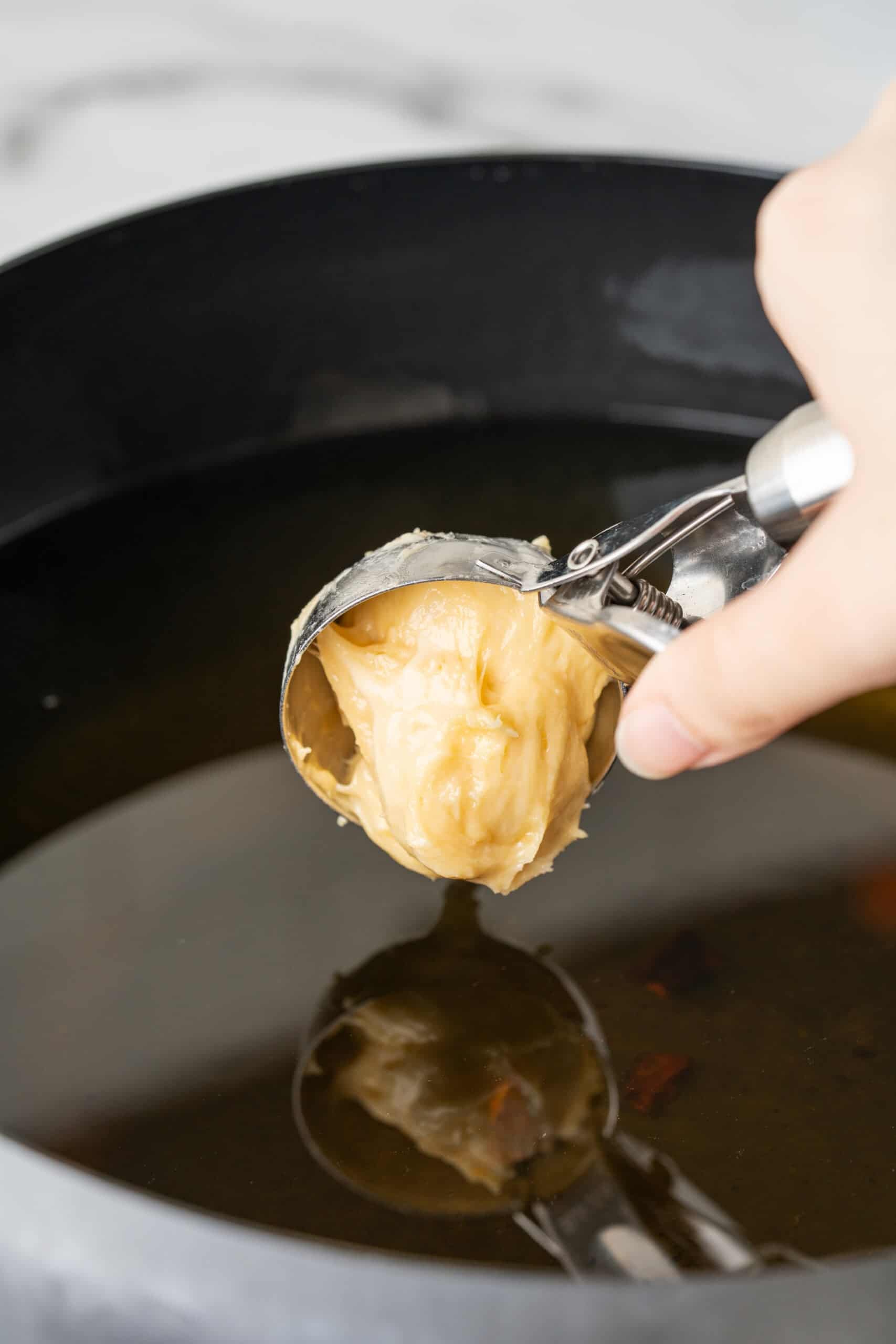 Hand holding a scoop of dough over a pot of hot oil, preparing to fry donut holes.