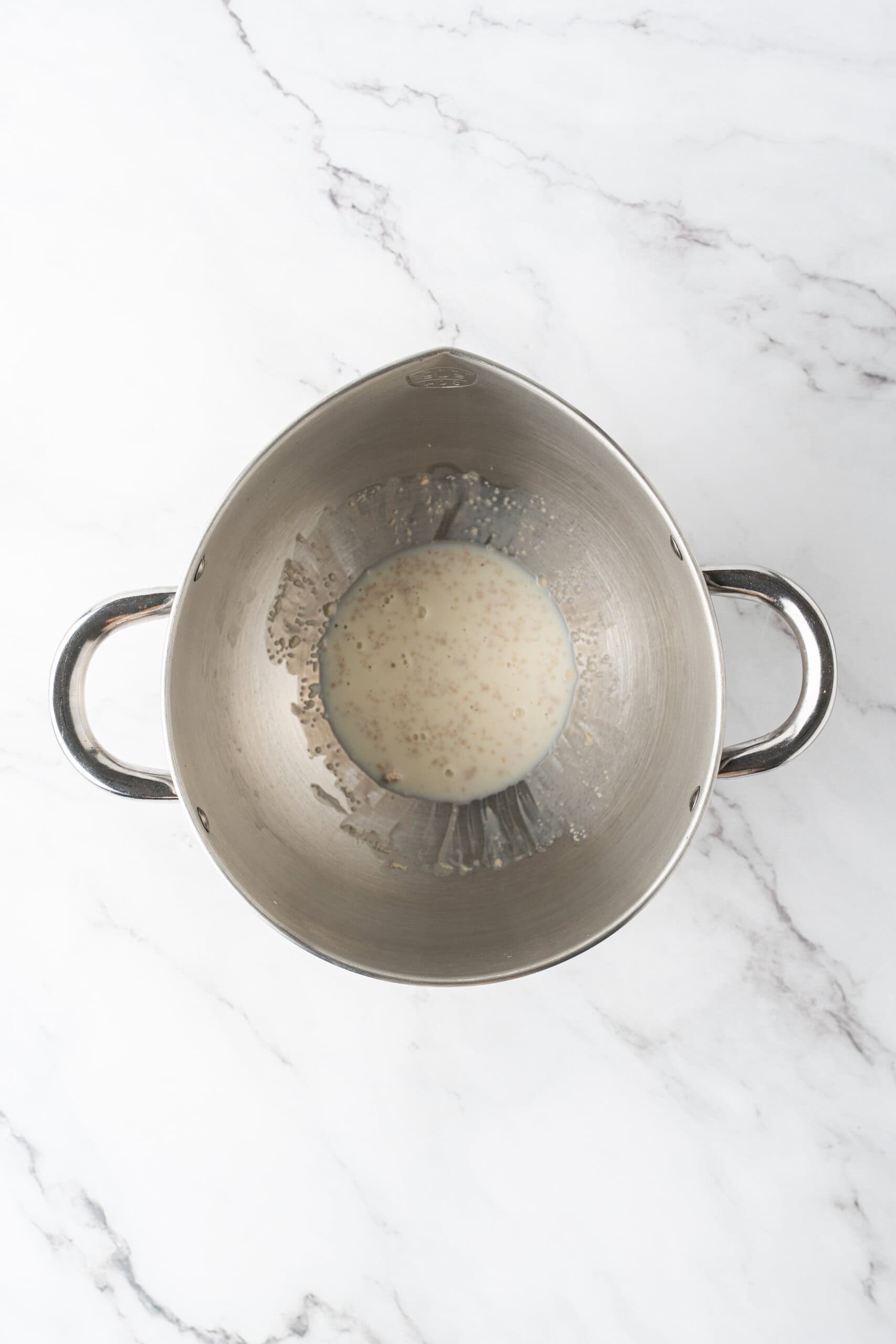 Yeast and milk mixture in a metal mixing bowl on a marble countertop