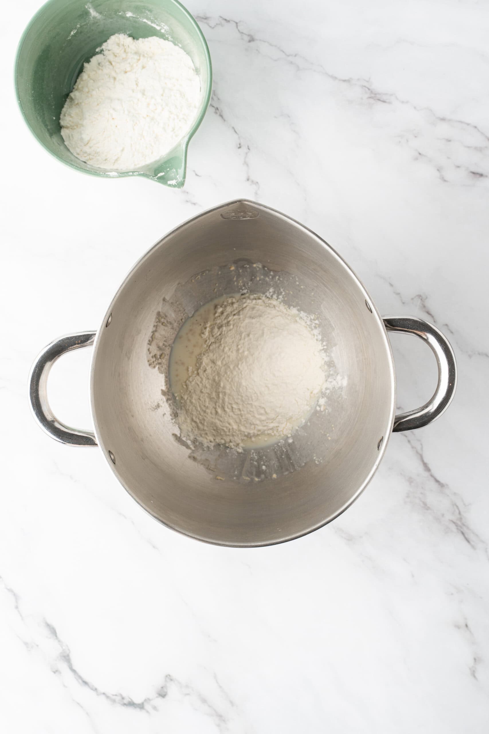 Bread flour added to a yeast and milk mixture in a metal mixing bowl