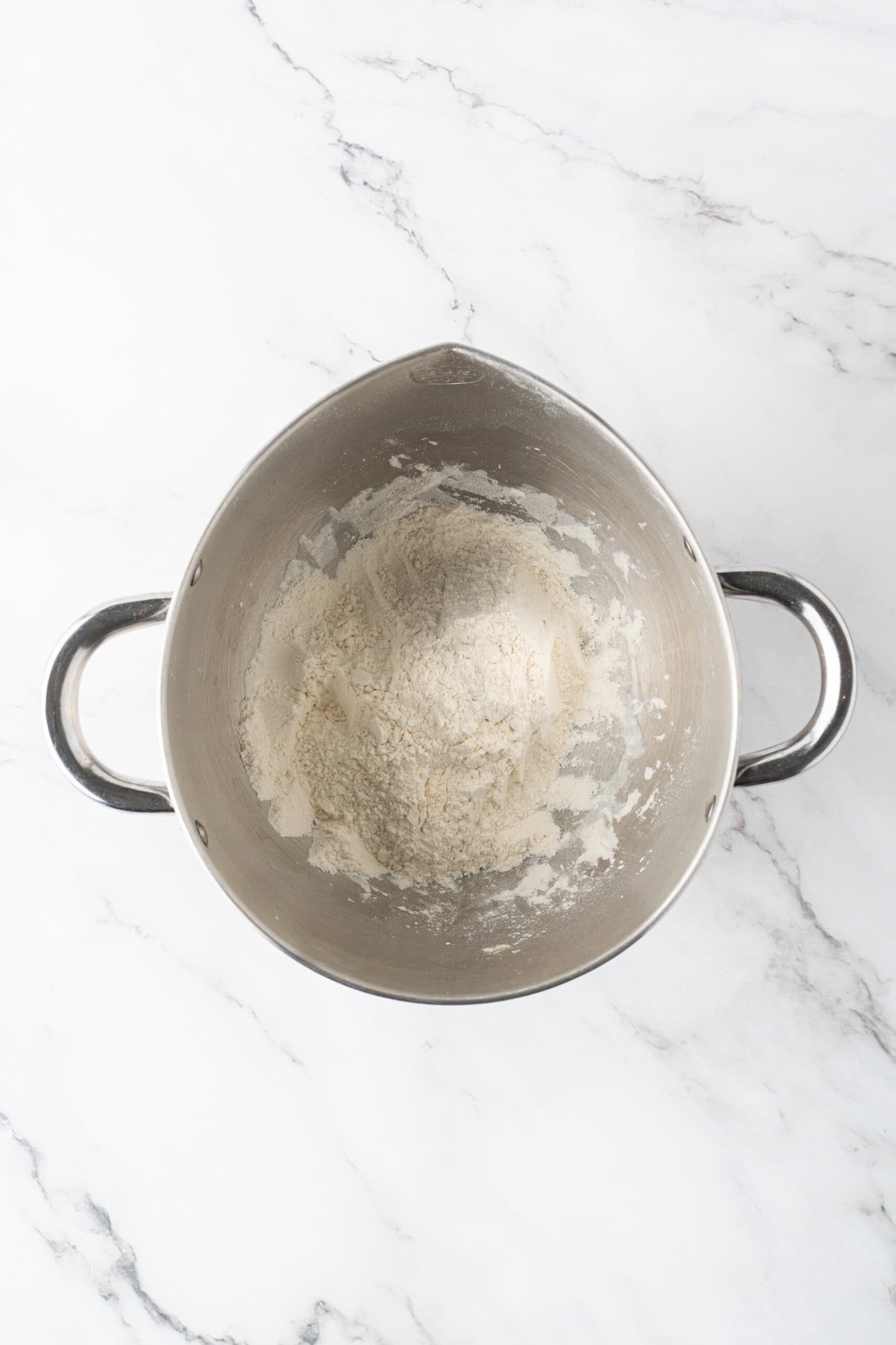 Dough mixture topped with the remaining dry ingredients in a metal mixing bowl