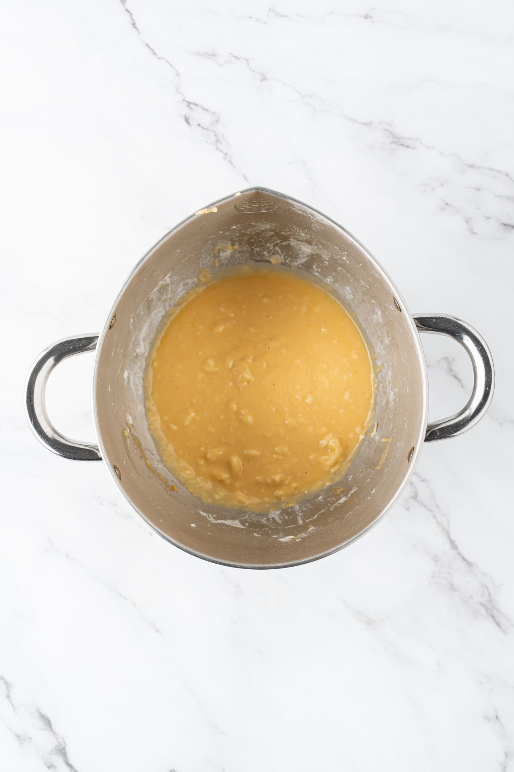 Dough mixture in a metal pot on a marble countertop.