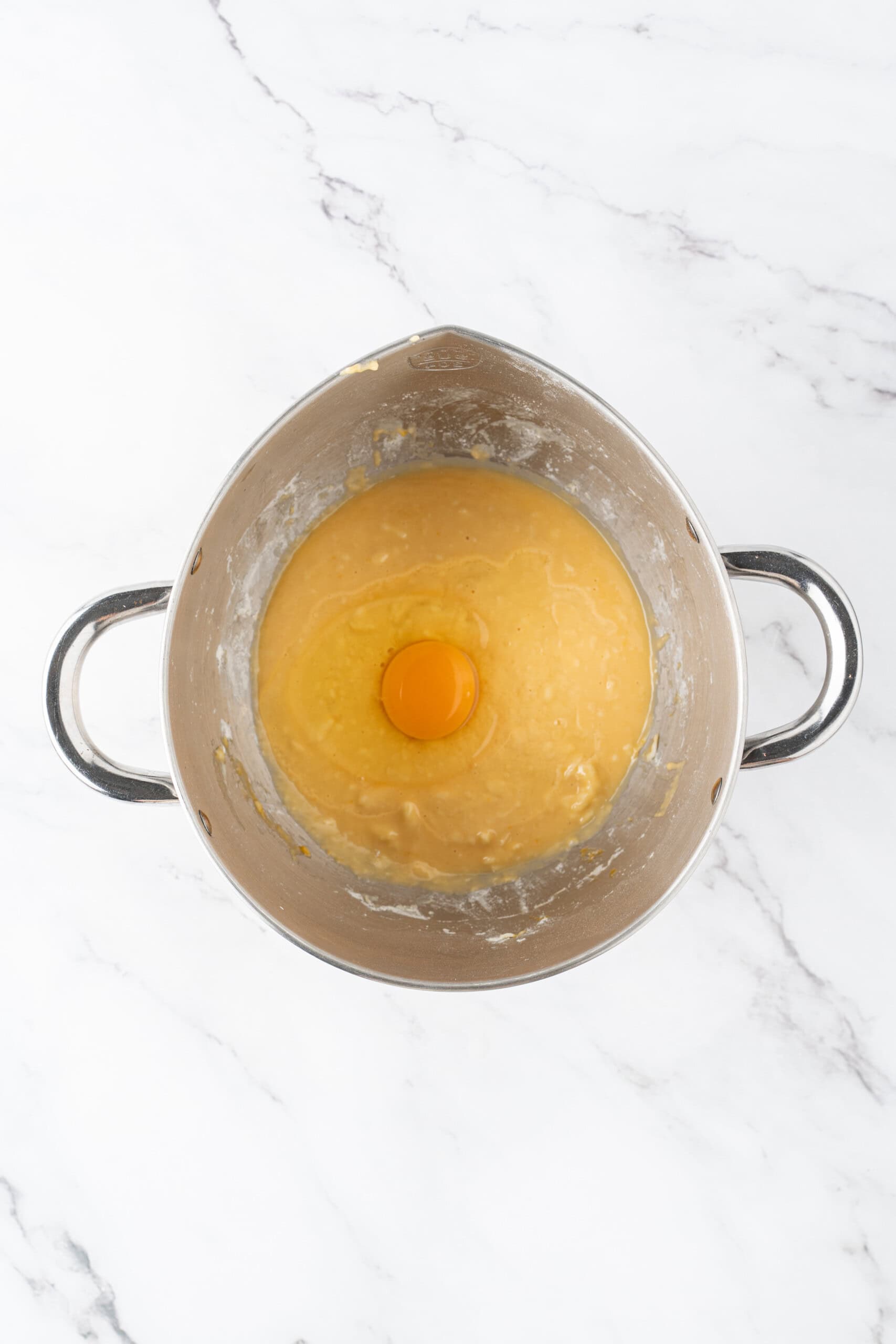 Egg added to a bowl of dough mixture in a metal mixing bowl