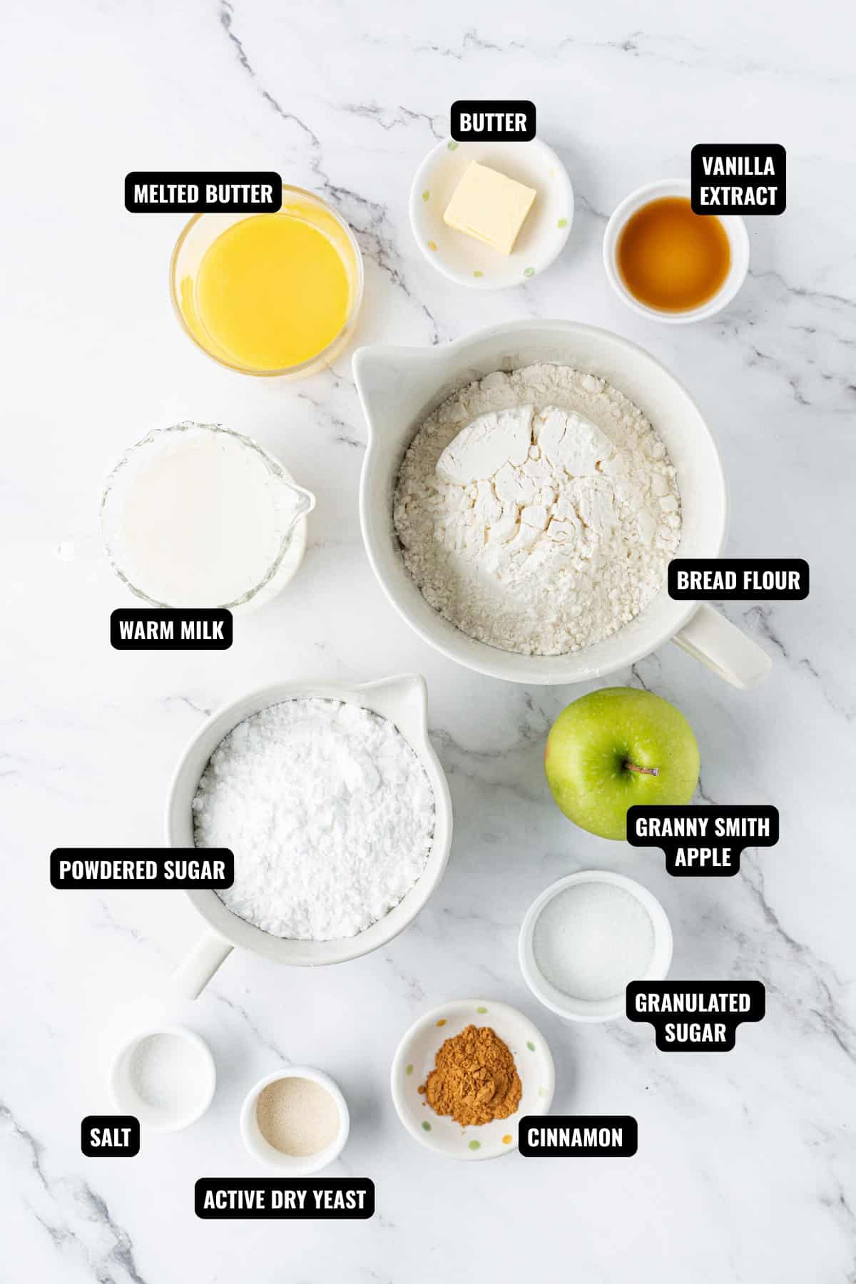 ingredients for apple fritters recipe including bread flour, butter, vanilla extract, milk, yeast, apples, powdered sugar, cinnamon, and sugar