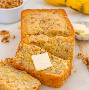 Banana nut bread sliced and served with butter, featuring a moist texture and crunchy walnuts.