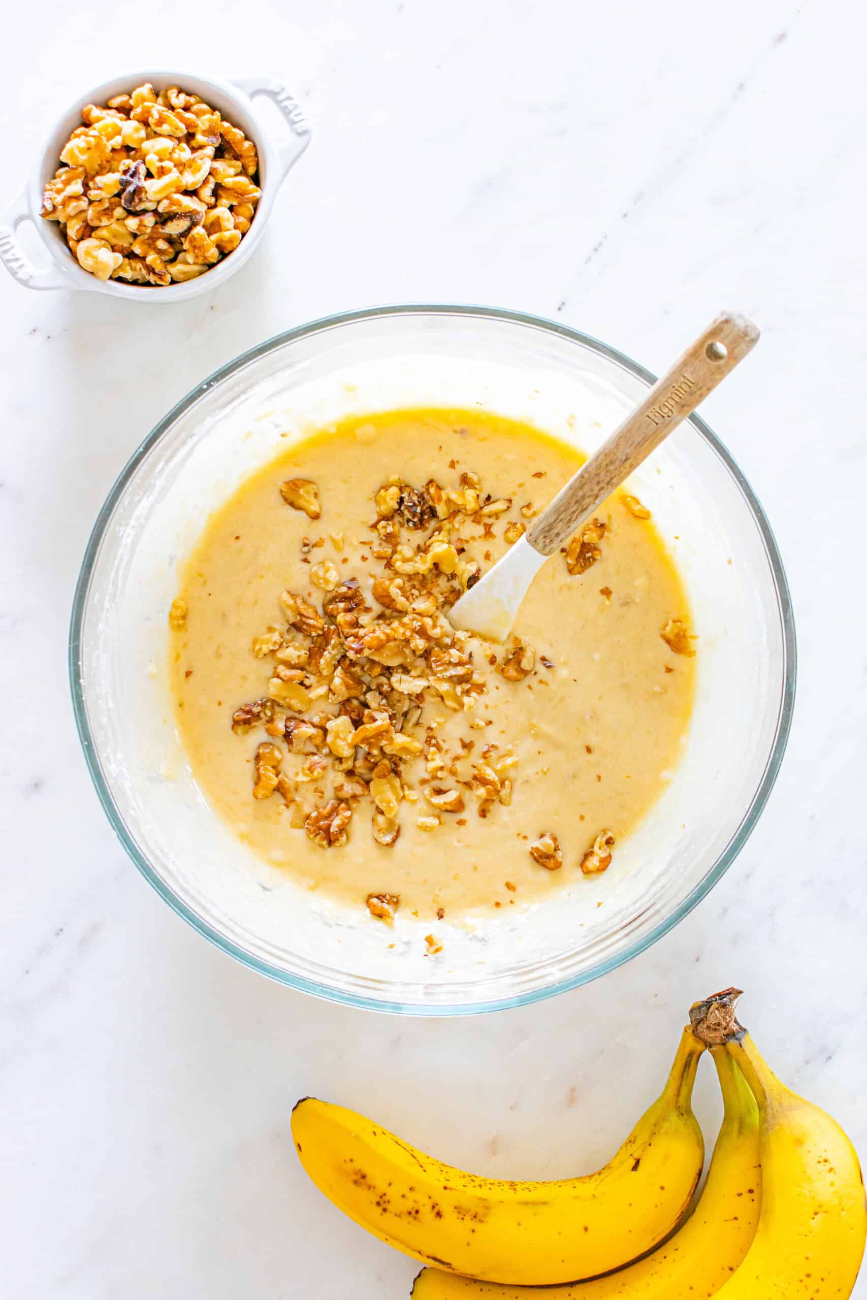 Banana bread batter with chopped walnuts in a glass mixing bowl