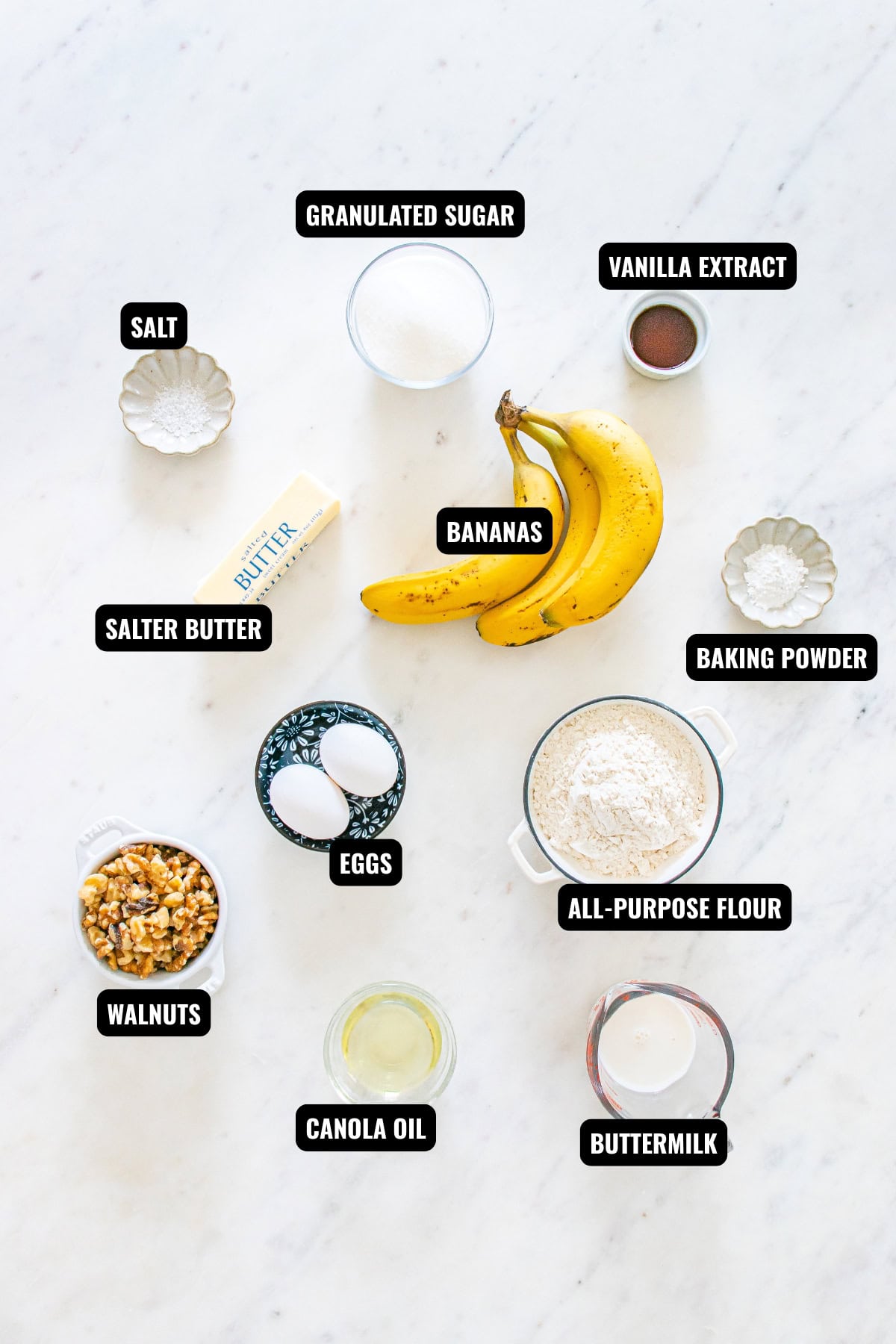 ingredients for banana nut bread recipe including bananas, butter, eggs, walnuts, buttermilk, canola oil, all-purpose flour, sugar, vanilla extract., and baking powder.